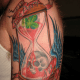 An hourglass tattoo with blood, skull, wings, and four-leaf clover.
