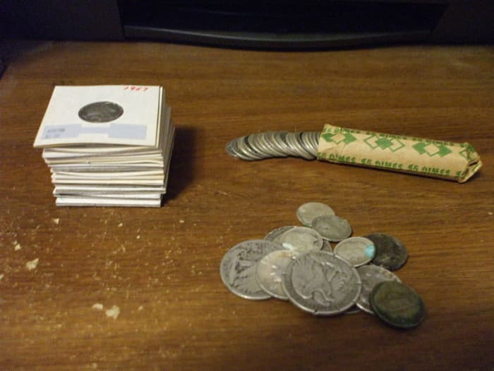 P. Domain. US coinage pictured is ineligible for copyright. Junk silver in the form of Pre-1964 US Coinage. From top left: Silver dimes in paper holders, a roll of dimes and a mixed-loose lot of half dollars, quarters, dimes and "wartime" nickels.