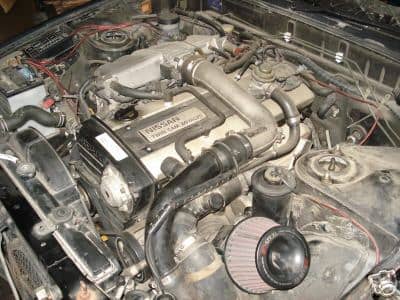 OEM RB20DET intake manifold on left, with crossover pipe and OEM side mount intercooler piping visible. The stock cross over pipe (the L shaped pipe which travels above the spark plug area) suffers from heat soak under the best of conditions.