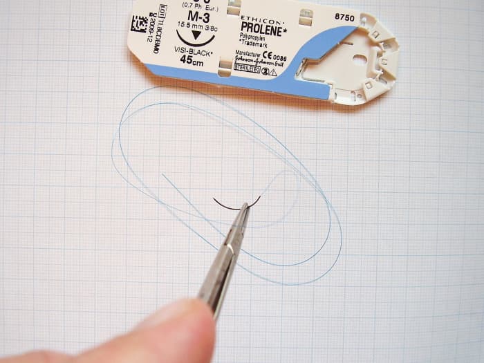 An atraumatic (swaged) needle and attached thread held in a needle holder; in this case, the suturing needle is curved