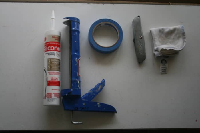 The white bath/kitchen caulk, the gun, blue painters tape, utility knife, and a washcloth. Missing is the paper towels, which come in quite handy for cleanup.