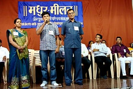 A marriage candidate introduces himself in a get-together arranged by a marriage bureau. His parents stand beside him.