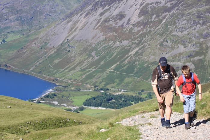 A father and son climbing up the trail towards the summit of Scafell Pike with the deep blue Wast Water and Wasdale in the distance