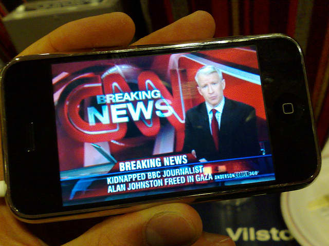 An iconic image of a breaking news broadcast is displayed on the smartphone.
