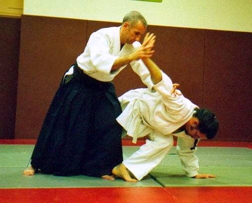 A teacher wearing a hakama executing an Aikido technique on a student wearing a gi.