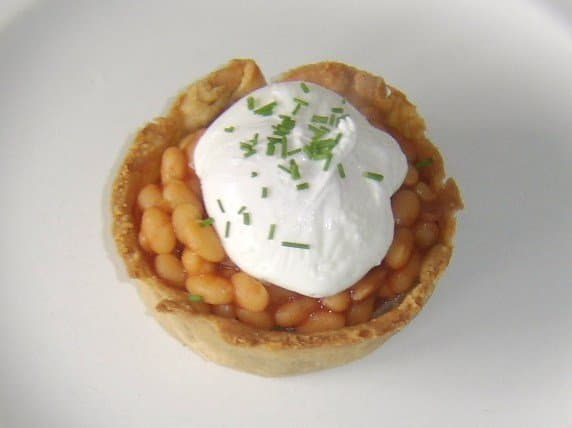 A homemade Scotch pie topped with baked beans in tomato sauce, a poached egg and some freshly chopped chives