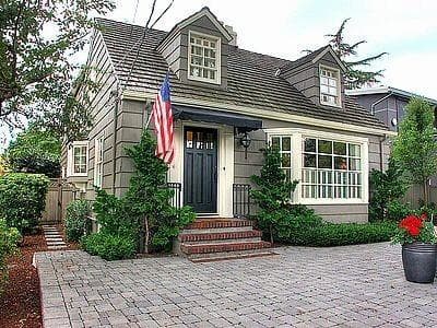 Asymmetrical front door, brick steps, bay window, two dormer windows, and an American flag
