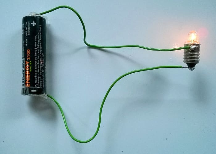 In this example of a simple circuit, an AA cell forces current through the wires and lights up a bulb