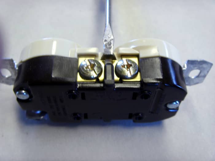 The screwdriver is resting on the tab to be broken. Make sure you're working near the screws that are brass-colored.