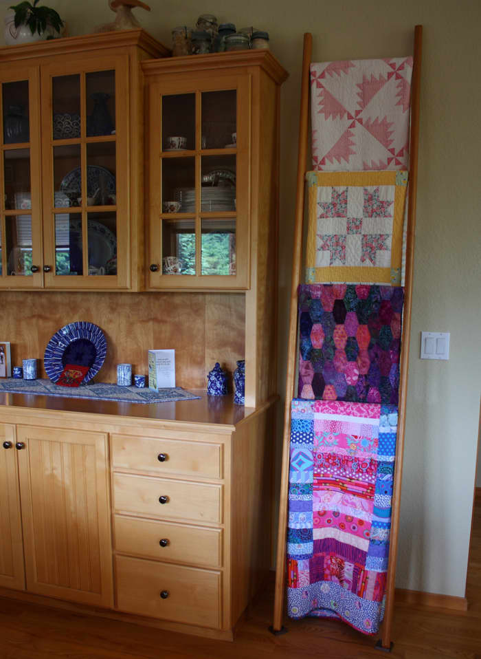 A table runner protects the furniture, and the quilts on the ladder display decorate the dining room while they wait to be called to use.
