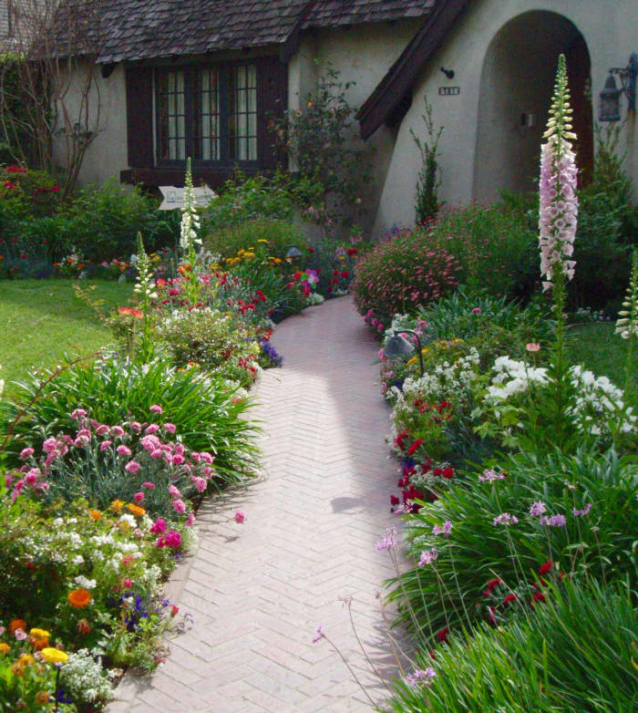 English Country Cottage style. Note the abundance of colorful flowers leading the eye toward the front door. The foxglove in the right rear typifies English style gardens.