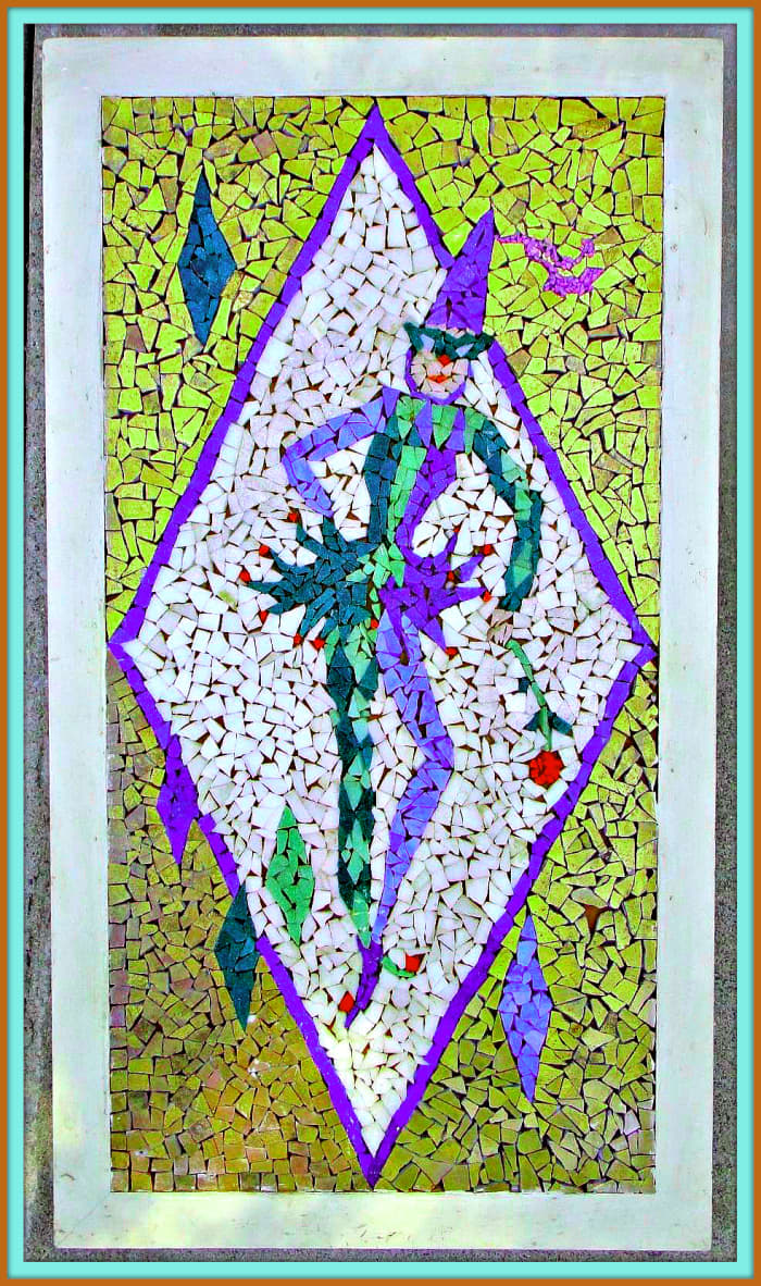 A vintage mosaic tile wall hanging from the 1950s featuring a jester / harlequin striking a pose with one hand on the hip, while the other is holding a rose. Framed in a wooden frame. Tile colors are white, green, purple, gold, and red.