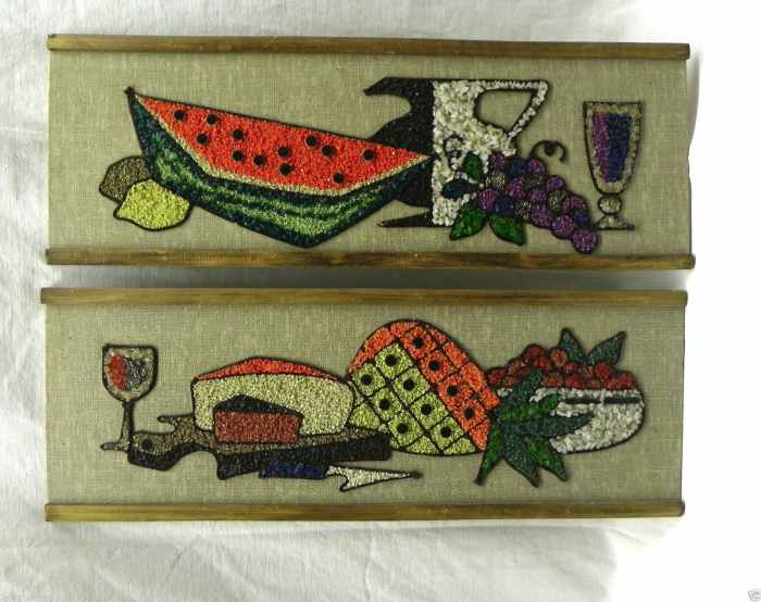 This is a set of two gravel art pictures in excellent condition. It has a beige woven fabric background mounted on Masonite with a wood frame on two sides. The mosaic features a still life arrangement with a wine goblet, cheese wedges, and fruit.