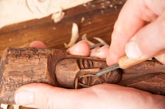A small wood gouge being used to create an intricate facial image in wood.