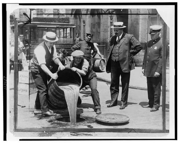 New York City Deputy Police Commissioner John A. Leach, right, watching agents pour liquor into sewer following a raid during the height of prohibition.