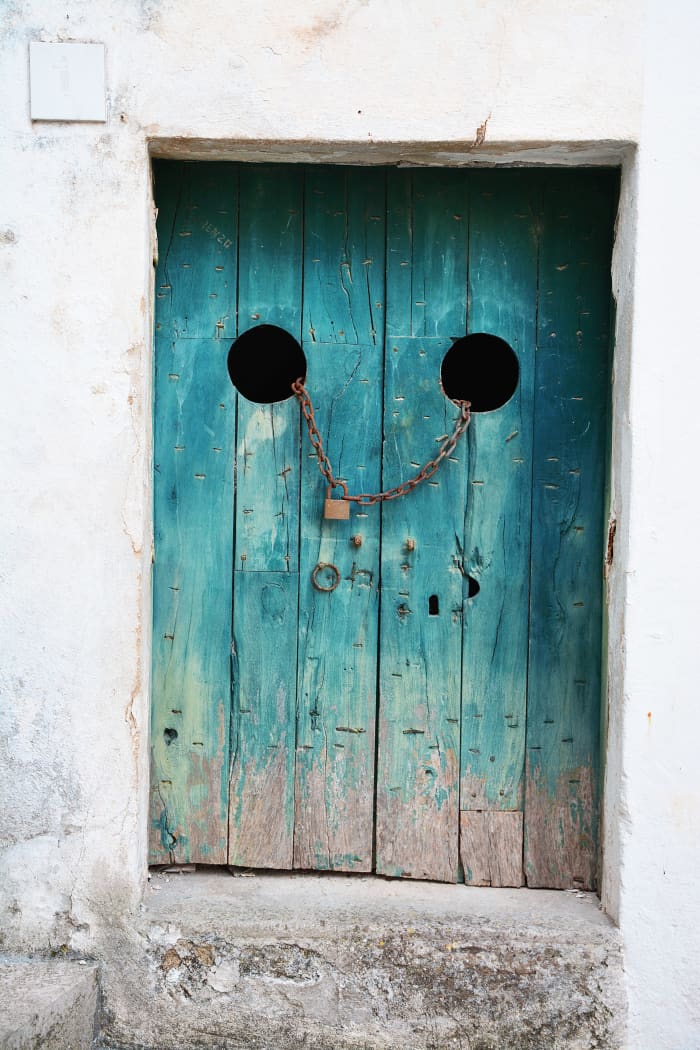 A bright teal door set in a white building. It's locked with a chain going through the doors, and the paint is worn off near the bottom. What could be on the other side?