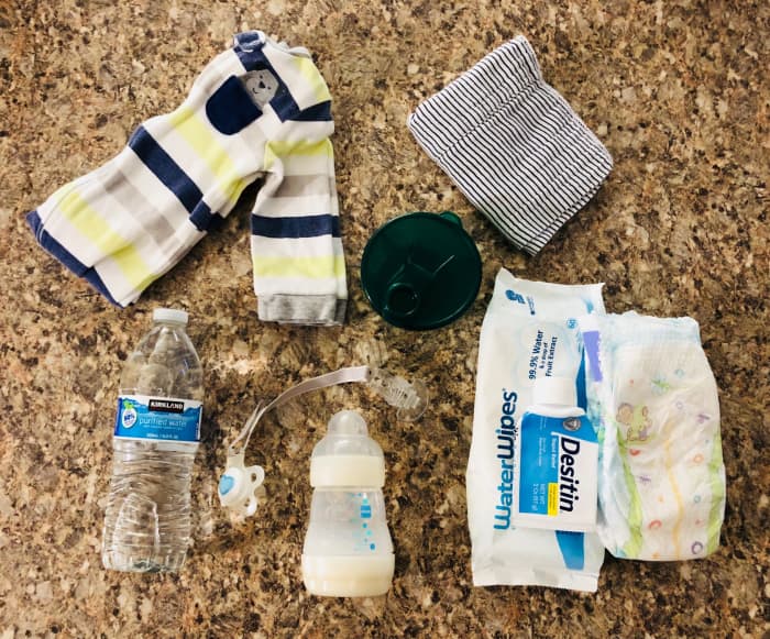 My Car Ride Essentials: Extra Onesie, Rag, Formula Dispenser, Bottle of Water, Bottle, Pacifier, Wipes, Diapers, and Rash Cream.