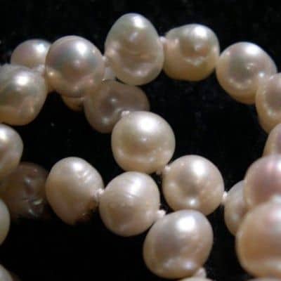 Telltale signs include surface imperfections, shape irregularities, color gradients in the nacre, luster, and the knots between each gem.