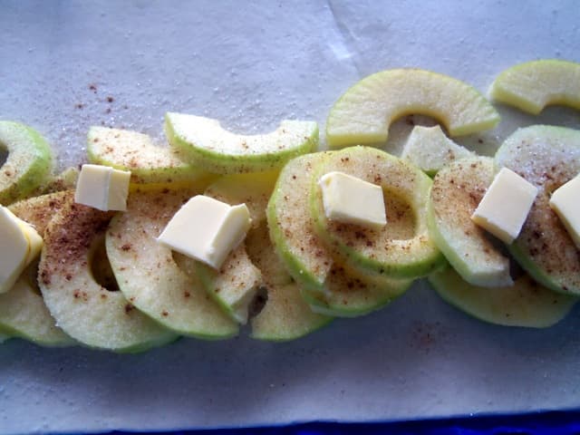 Lay out a row of apples and sprinkle with cinnamon and sugar. Add the cubes of butter.