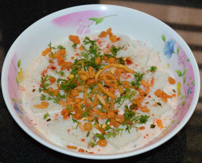 Step three: Add a thin layer of titbits such as a mixture or broken chips to it. Garnish with finely chopped coriander leaves and red chili powder.