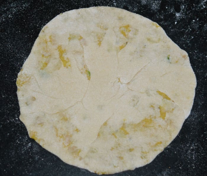 Step five: Place a portion of the stuffing in the center. Bring the edges of the disc together and close the open ends. Press it a little. Dust it with wheat flour and roll it to make a disc of about 7-8 inch diameter.