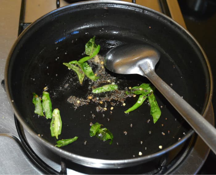 Step three: Heat oil in a deep-bottomed pan. Throw in mustard seeds. Let them crackle. Add hing powder, slit green chilies, and curry leaves. Saute for 30 seconds.