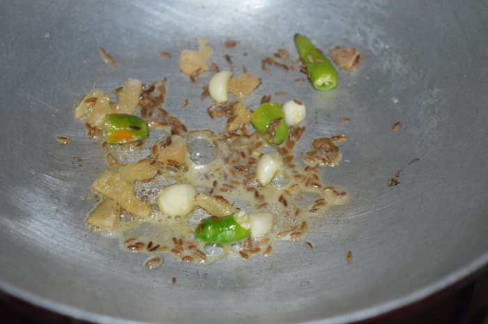 2. Heat 1 teaspoon oil in a deep-bottomed pan. Add cumin seeds. Allow them to crackle. Throw in garlic, green chilies, and ginger. Saute for a few seconds.