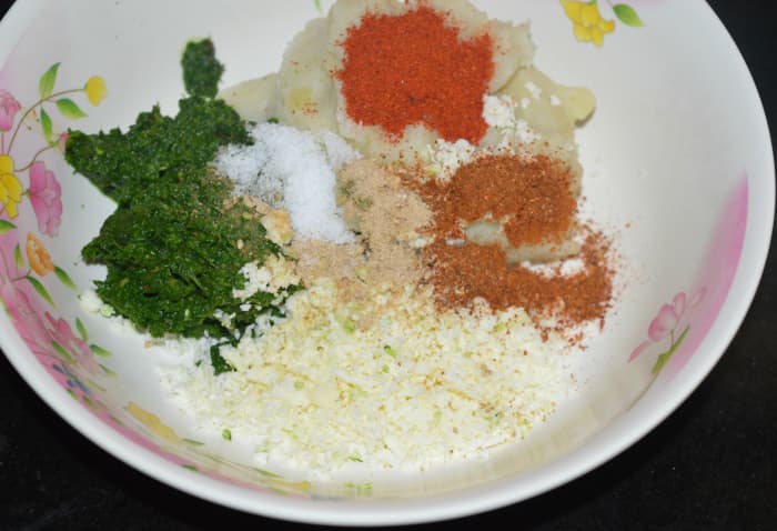 4. Add the leafy greens paste, grated paneer, mashed potatoes, red chili powder, spice powder or garam masala powder, raw mango powder, and salt. Mix well to prepare a firm dough.