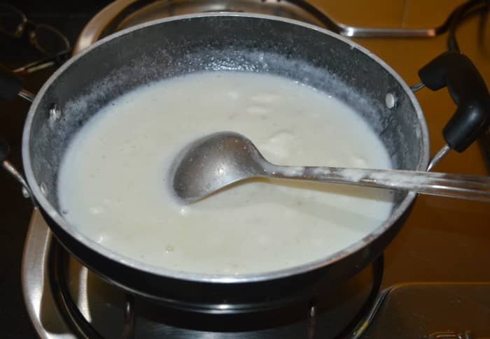 Step two: In a deep-bottomed non stick pan, add milk, coconut milk, sugar, and powdered cardamom. Turn on the stove. Keeping the heat at medium-high, stir the mixture frequently.