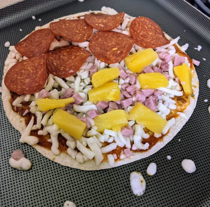 A pepperoni, ham, and pineapple pizzadilla begins cooking. Organizing toppings across an open tortilla makes it easier to fold and helps ensure your toppings are evenly spread.