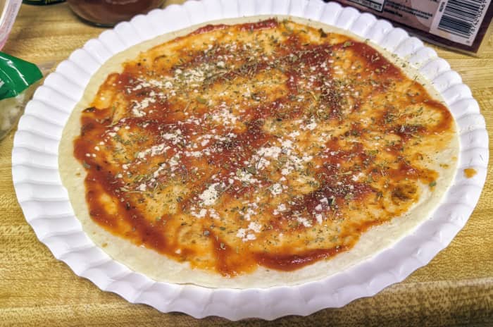 The base of a pizzadilla features sauce and seasonings. Above, a plain tortilla shell is prepped with traditional pizza sauce, garlic powder and Italian seasoning. Another delicious option is to sprinkle on half a Zap Pak from Little Caesars!