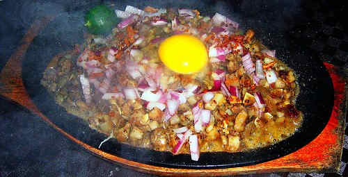 Sizzling hot platter of pork sisig with a raw egg on top