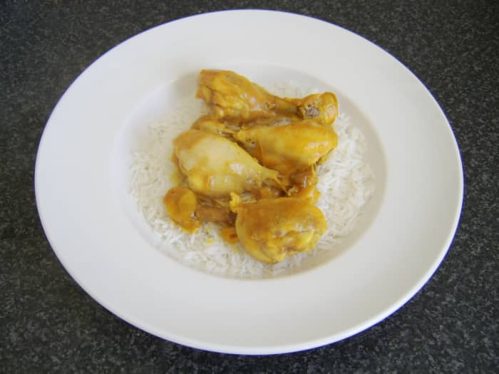 The chicken drumsticks are removed from the casserole and laid on the bed of rice before the curry sauce is spooned over the top