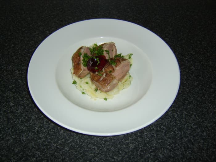 The pan-fried duck breast is rested before being sliced and served on the bed of mash, garnished with parsley and red currant jelly.