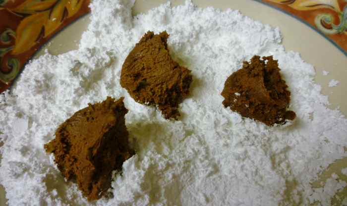 Dropping bits of the cookie batter into powdered sugar and then rolling into a ball shape.