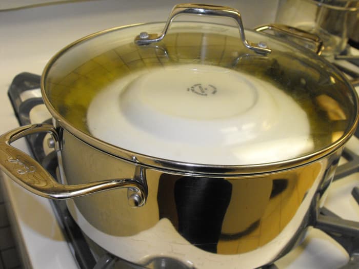 In this final photo, I show the sarma ready to cook on the stove top. Covered first with a couple layers of leaves and then with an inverted plate (to keep the leaves from floating), you add water (just one layer less than the top layer of sarma).