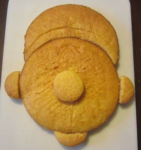 One round cake will be the main face, while the other will be cut to form the hat. The cupcakes will form the nose, ears, and chin.
