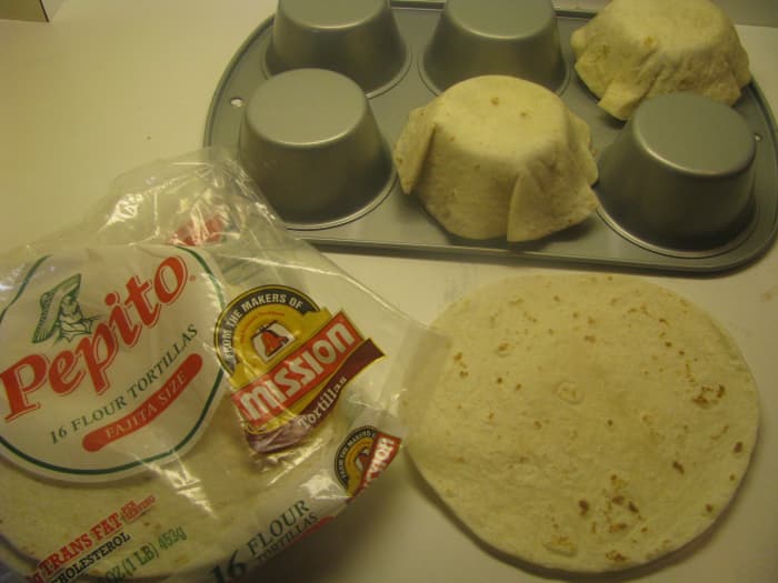 Step Two: Turn the muffin tin upside down and place one tortilla shell around each cup of the muffin tin. Gently mold it around the cup with your hands. Note: A muffin tin is larger than a cupcake tin. A cupcake tin is too small for this recipe.