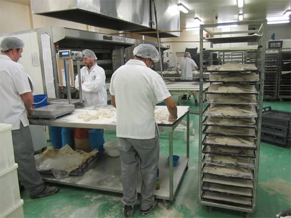 Loaves being shaped to be placed on trays on racks for final rise. 