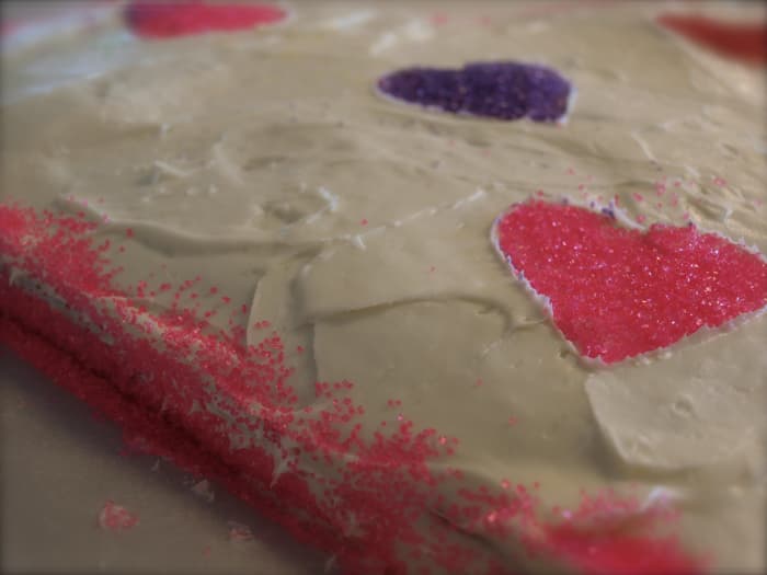 Using decorations of your choice, decorate the cake. To get the glitter hearts, I used a heart-shaped cookie cutter and gently laid it on the cake surface. Then I added glitter to the center of the cutter.