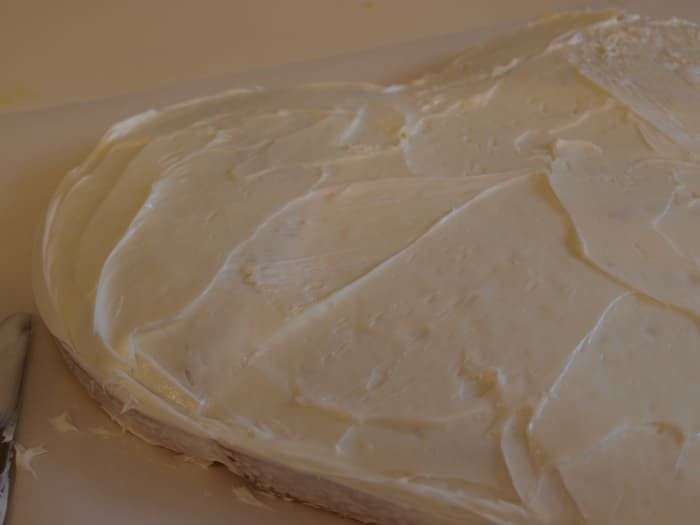 Using the tub of frosting, frost the cake. Begin by applying a thin frosting layer on the cut edges of the round cake and adhere them to the square. Continue frosting. If the layers are not the same height, use frosting to even out the surface.