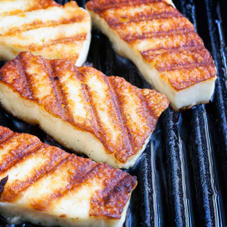 Searing halloumi cheese in a grill pan. Halloumi is a good choice for this type of frying, as it has a thicker texture, making it less likely to melt.