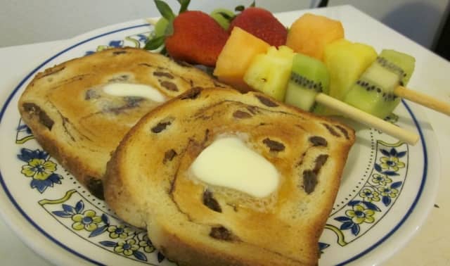 This serving suggestion for a light breakfast includes two fruit kabobs served with toasted, buttered raisin bread.
