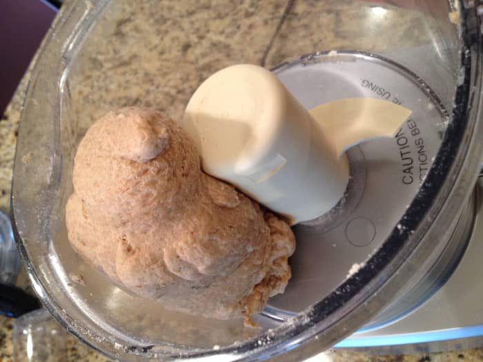 Combine hot water with olive oil in a measuring cup. Turn the food processor on and gradually pour in the liquid until the mixture forms a sticky ball. Add additional water or flour if needed.