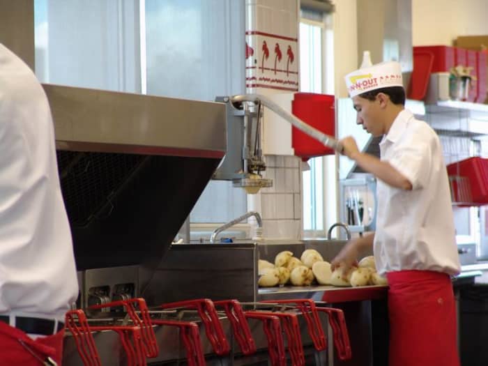 An In-N-Out associate dicing potatoes to make fries. In the back, other associates are probably cleaning and peeling potatoes which will be diced later.