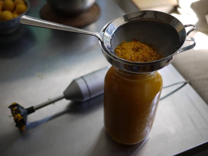 After blending again, strain solids from liquids: It helps to fit your strainer inside a funnel, as I do. The resulting syrup should be cloudy with fine particles of root.