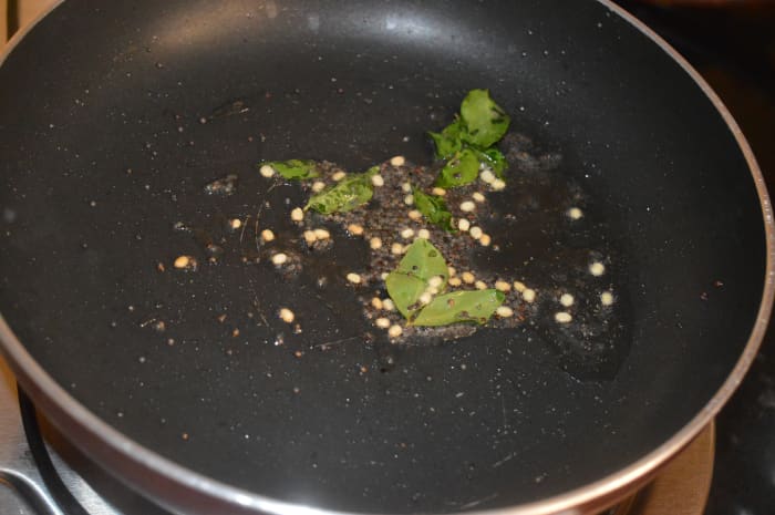 Step three: Heat oil in a deep-bottomed pan. Add mustard seeds, white lentils, and curry leaves. Saute till mustard seeds pop.