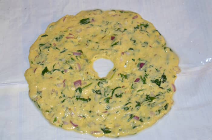Step 5: Divide the dough into four equal portions. Make a patty out of one of the portions on a greased plastic sheet. Apply water to your fingers and expand it to make a disc of about six inches in diameter. Make a big hole in the center.
