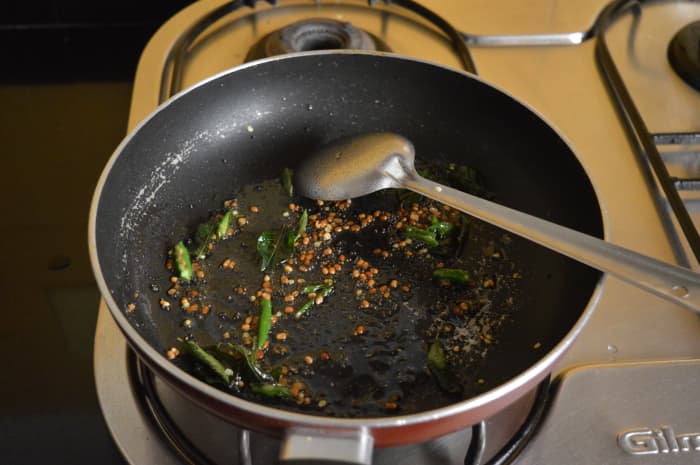 Step one: Heat oil in a pan. Throw in mustard seeds. Let them crackle. Add white lentils, curry leaves, and slit green chilies. Saute till lentils become golden brown.