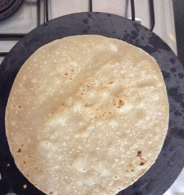 Once the Chapati starts changing color, flip it over. Let it remain on that side for a minute. Press and rotate it using a kitchen towel.